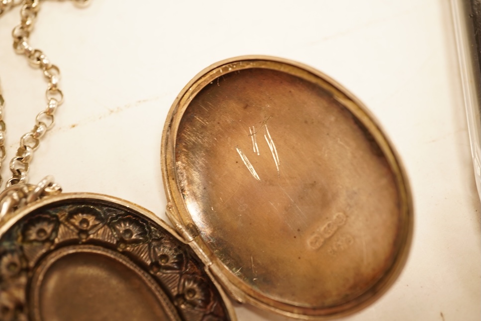 A late Victorian embossed and engraved oval silver locket, 42mm, on a later white meta belcher link chain, together with an Edwardian silver and hardstone inlaid pill box, now with pendant mount.